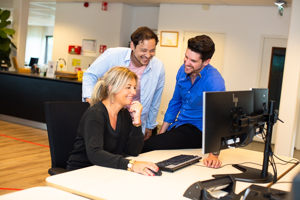 Drie collega's lachend achter een computer