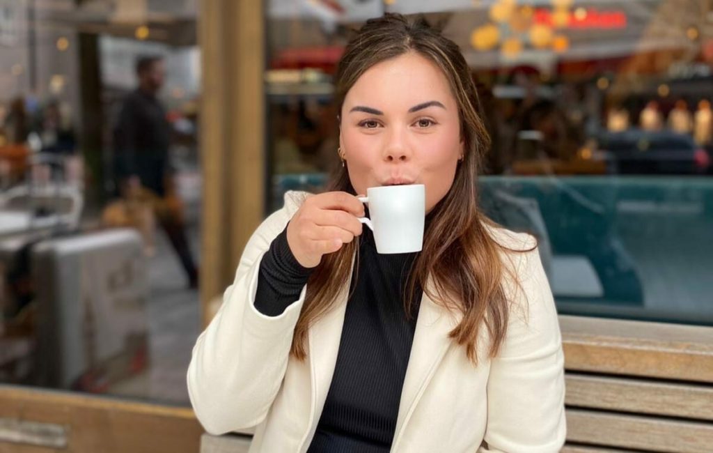 Vrouw met donker lang haar en wit jasje blaast in haar koffie.