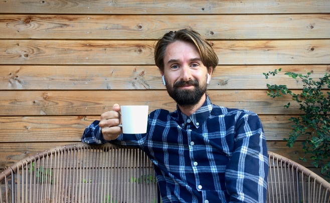 Man met baard en oortjes in zit met koffie op een bankje.