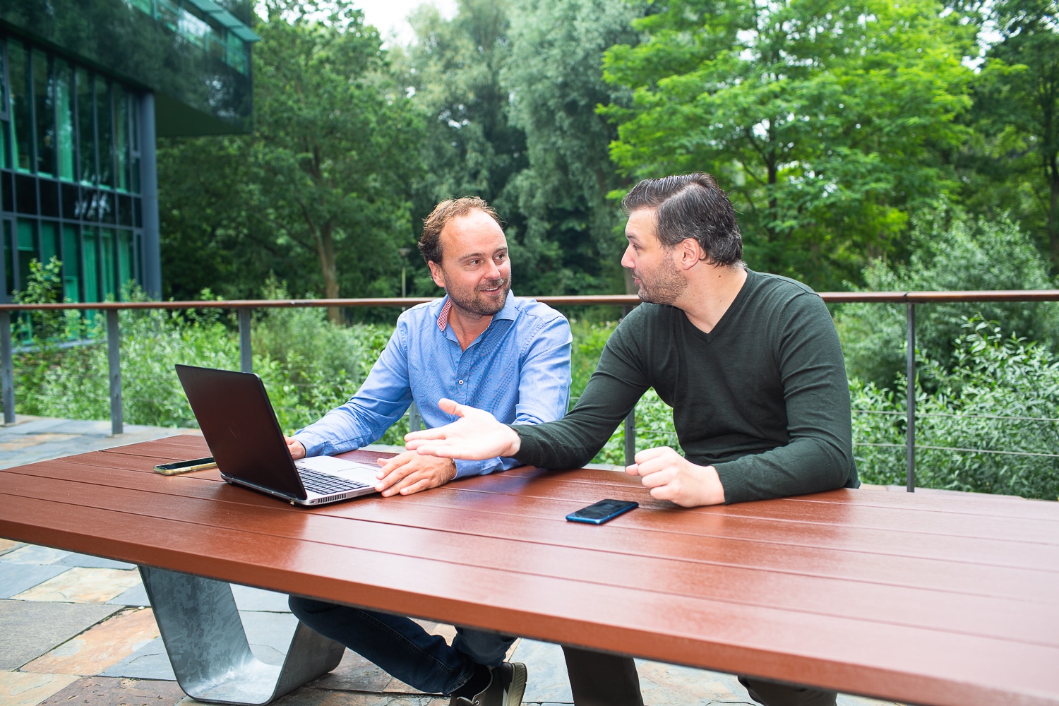 Collega's buiten aan een tafel met een laptop die overleggen