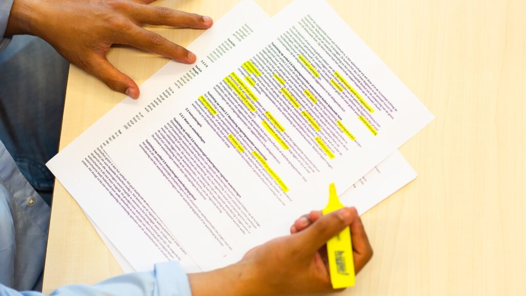 Iemand markeert met een gele stift in de hand tekst op een A-viertje