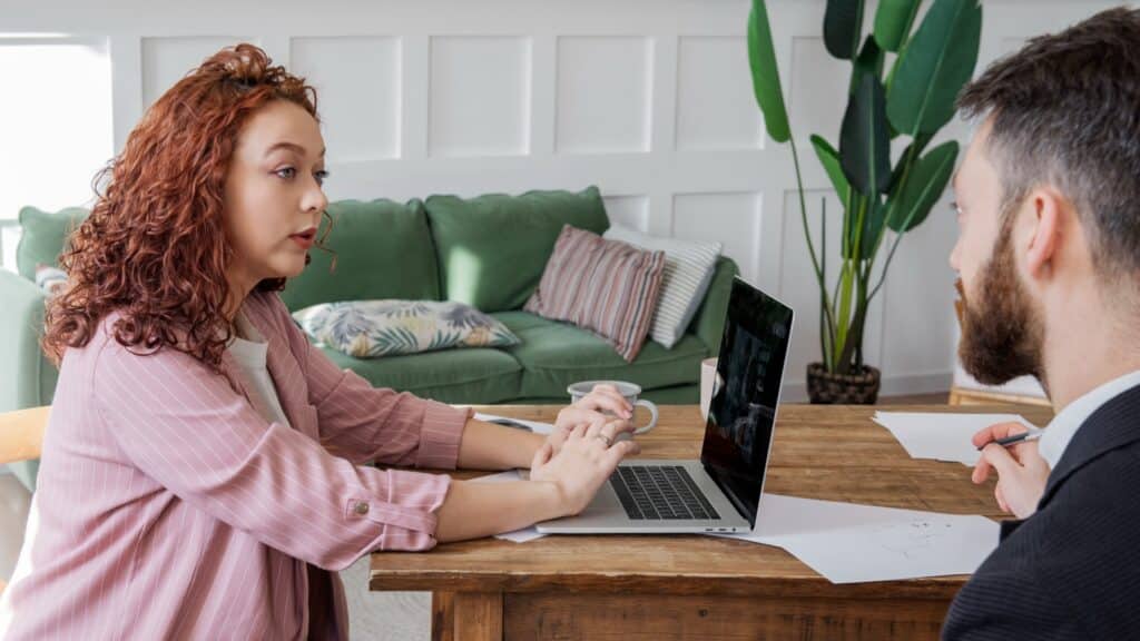 Twee personen hebben een gesprek bij een laptop.