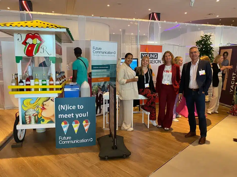 Collega's van Future Communication staan bij de stand op het beursplein. Er staan reclamebanners en een ijskar.