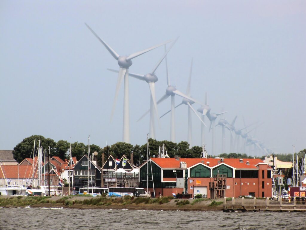 Meerdere windturbines aan de rand van een groot meer met daarvoor een haven en huizen