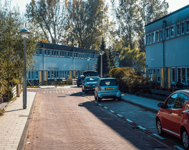 Een straat in een woonwijk met rijtjeshuizen aan beide kanten en auto's in de straat,